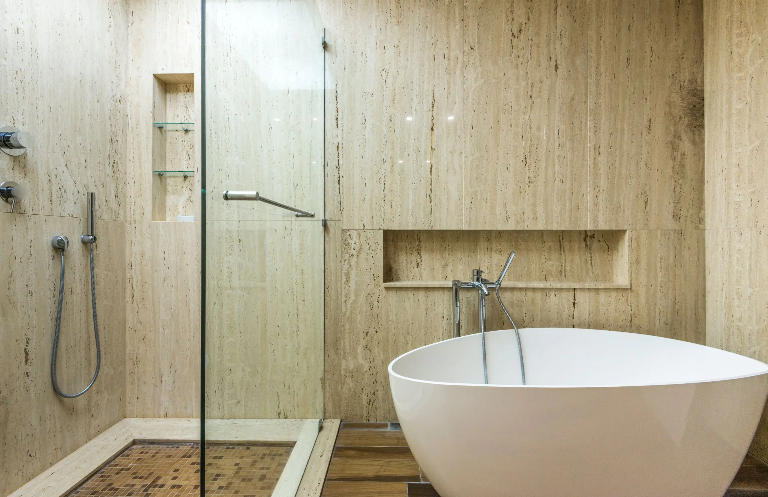A stone-tiled bathroom with a walk-in glass shower and a freestanding bath