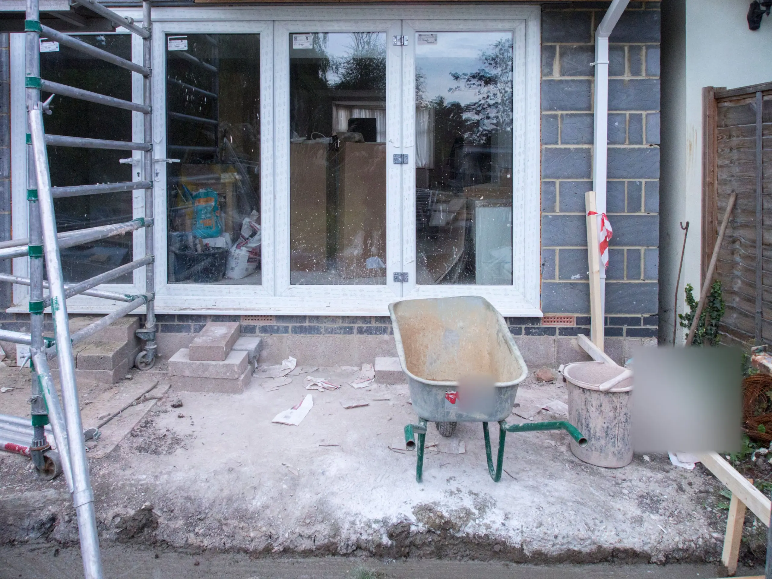 New glazed doors fitted in a blockwork rear extension, with a scaffold tower and wheelbarrow