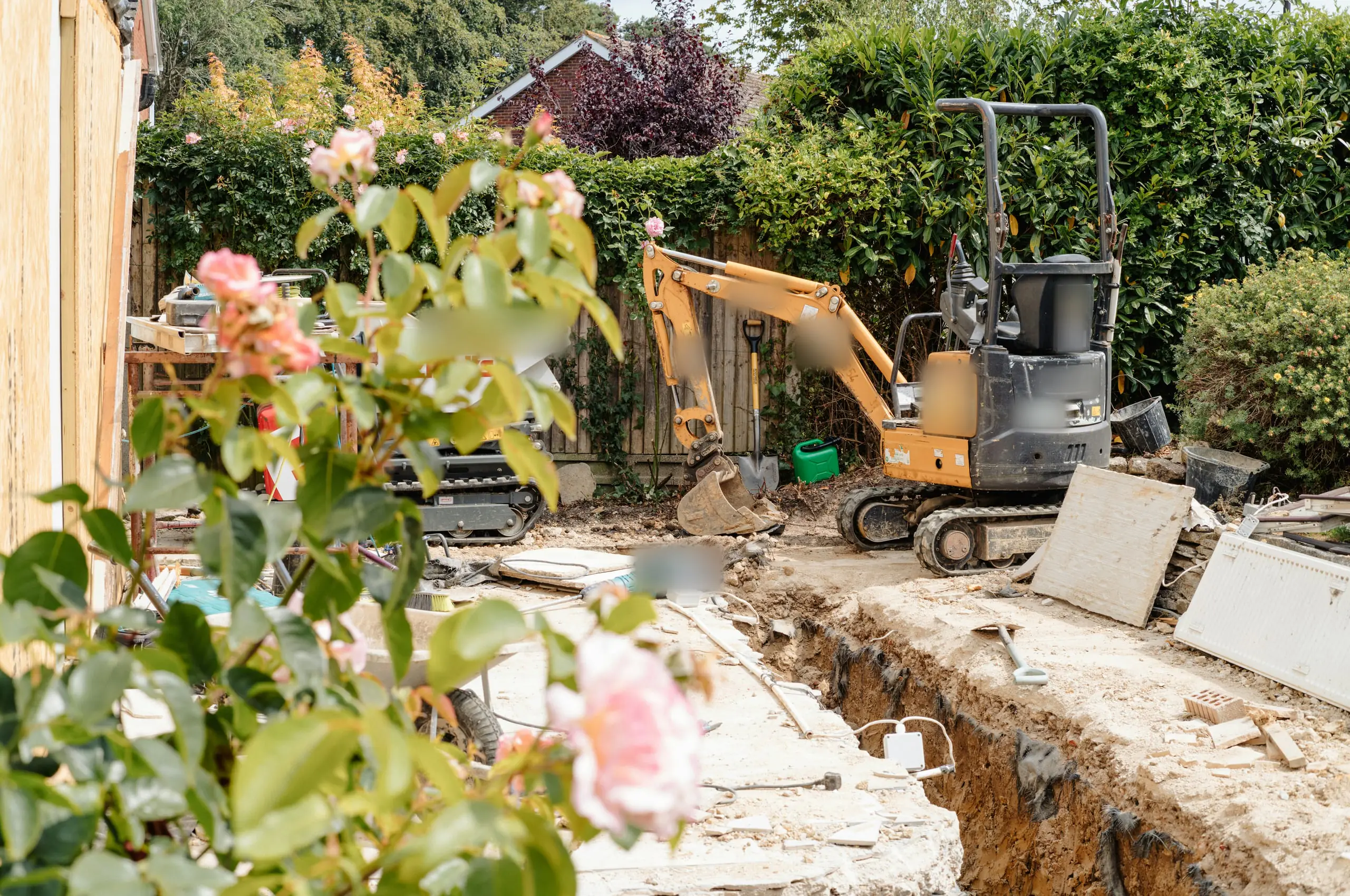 A mini digger beside a freshly dug foundation trench in a back garden