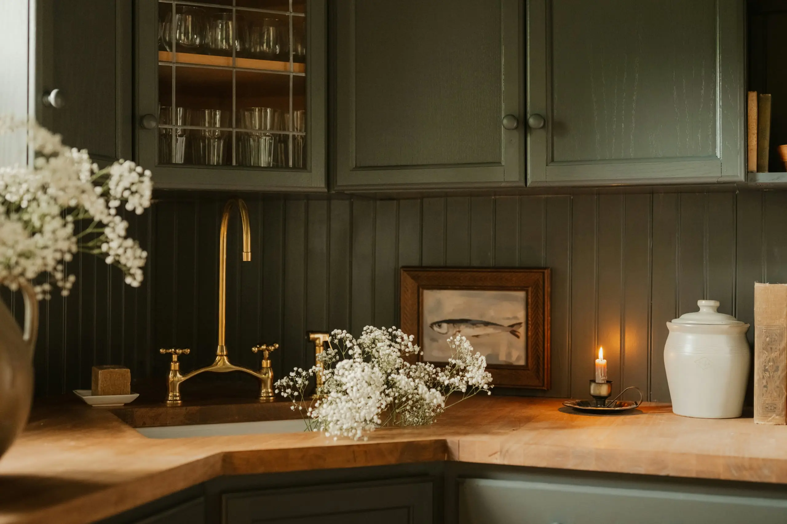 A deep green fitted kitchen with a brass bridge tap and wooden worktops