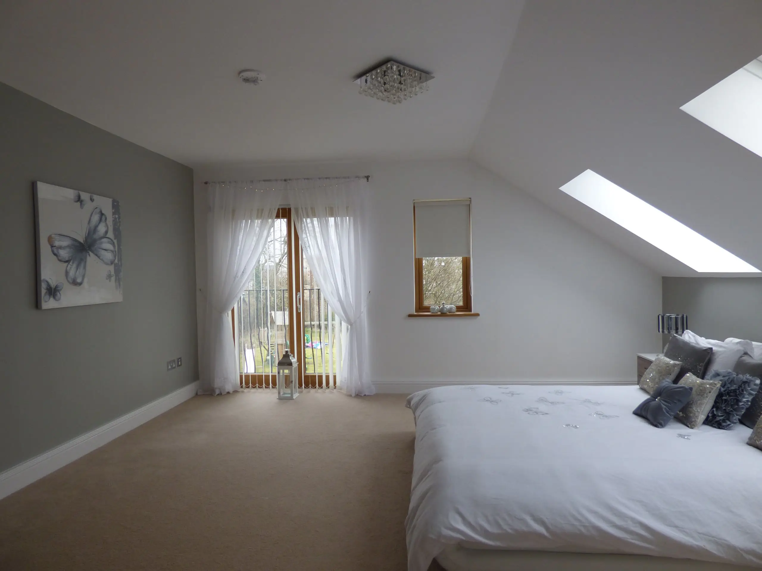 A loft bedroom with roof windows in the sloping ceiling and doors to a Juliet balcony
