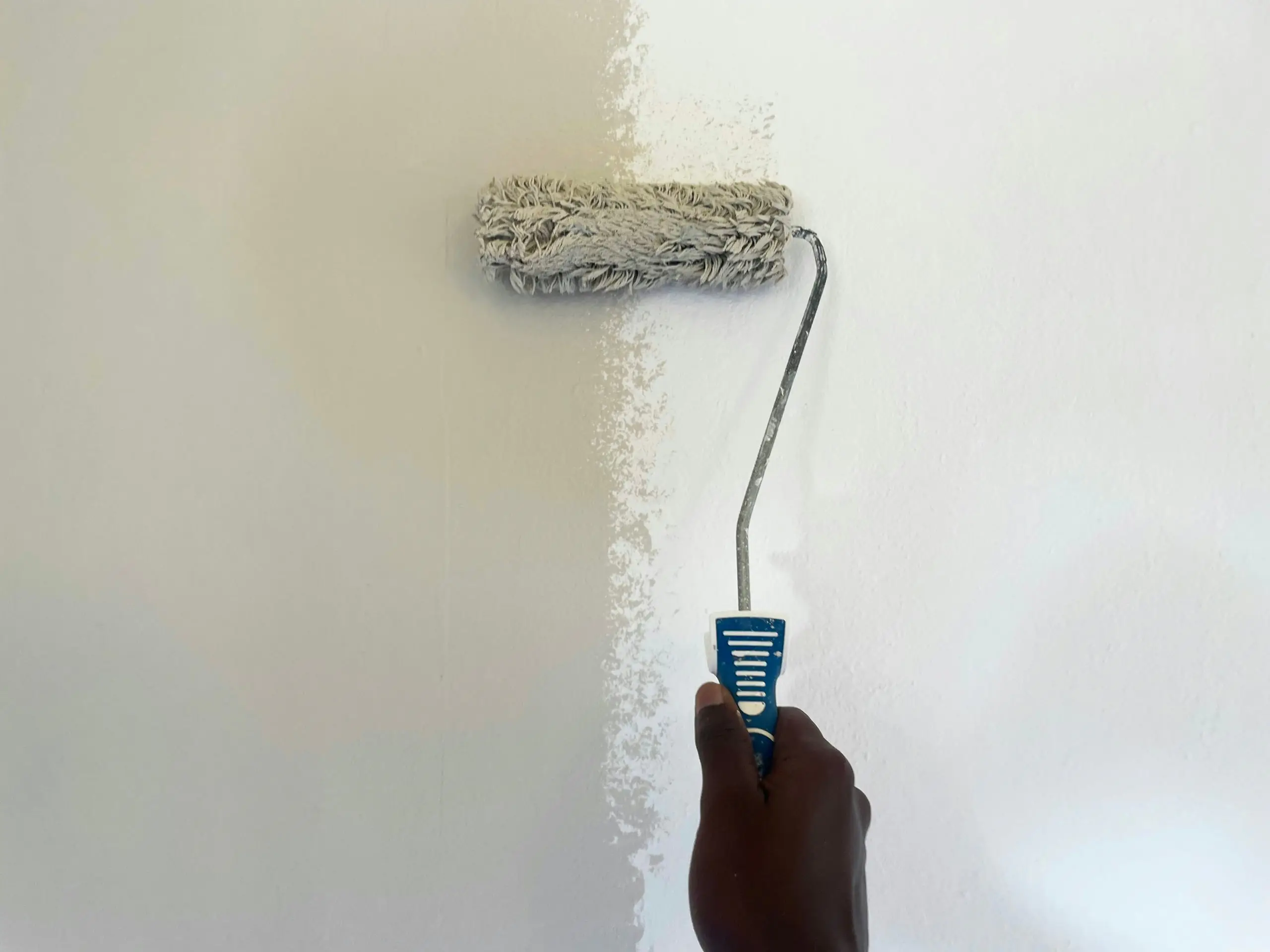 A hand rolling white paint over a cream interior wall