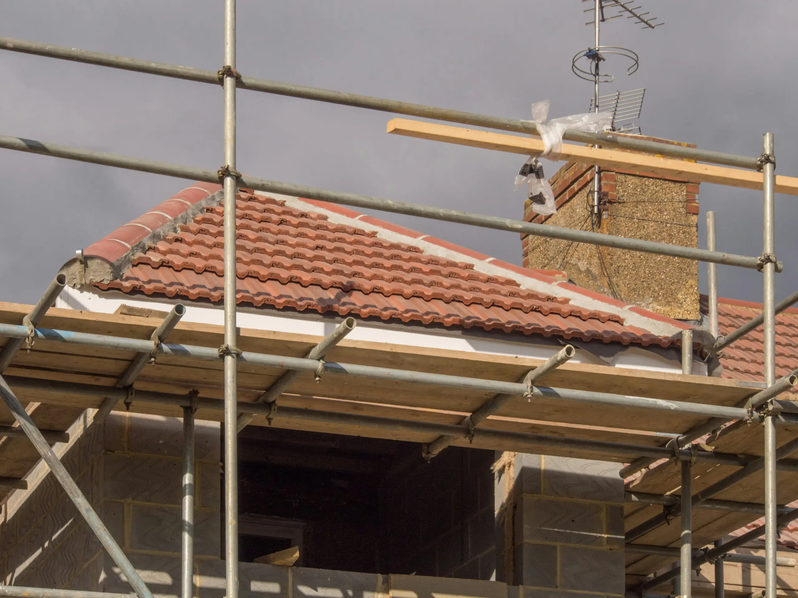 A newly tiled clay roof behind scaffolding, with a chimney and TV aerial